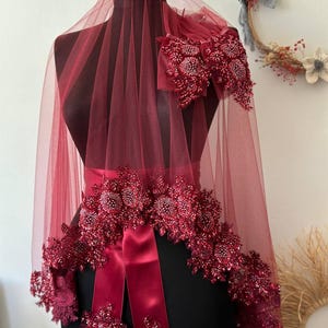 May include: A burgundy bridal veil with a satin ribbon and beaded floral embellishments.
