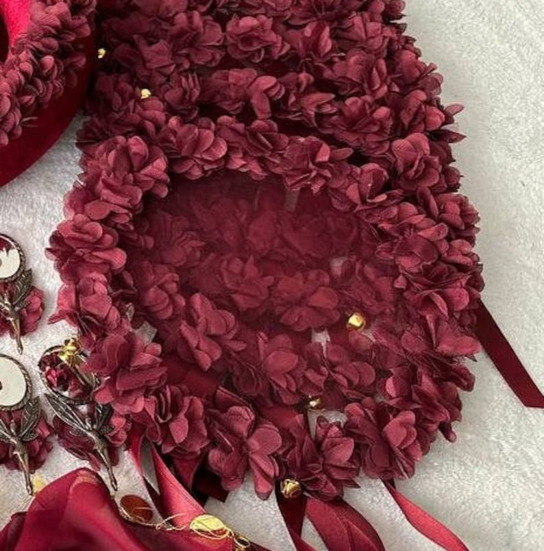 May include: A burgundy floral fabric with a sheer overlay and gold accents. The fabric is arranged in a circular shape and has a delicate, feminine feel.