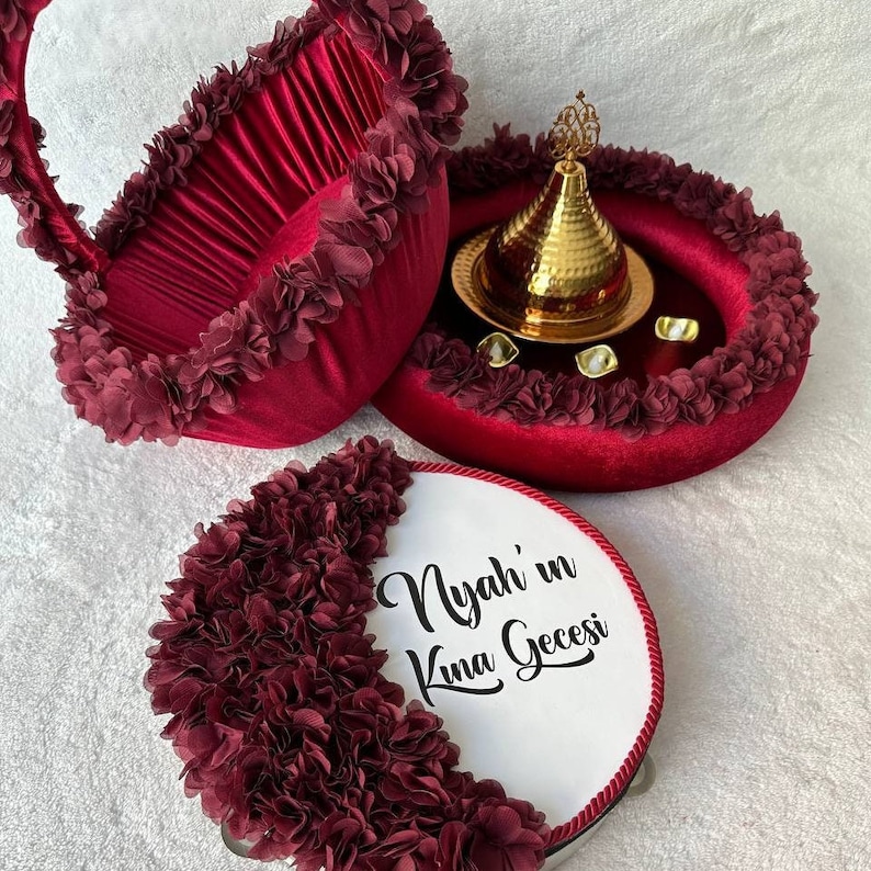 May include: A set of three decorative trays with a maroon velvet base and a ruffled maroon fabric trim. The trays are decorated with white text that reads "Nyah'in Kina Gecesi". The center tray features a gold metal decorative bowl with a gold metal lid.