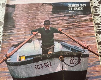 Puede incluir: Una portada vintage de la revista Boys' Life de abril de 1969 que muestra a un joven remando en un pequeño bote en un puerto. El texto de la portada dice "Fisher Boy of Spain, Page 22".
