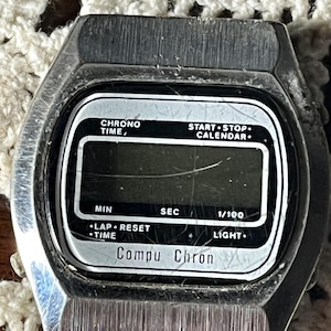 May include: Vintage Compu Chron digital watch with a silver-tone case and a rectangular black and white display. The watch face includes text such as "CHRONO TIME," "START STOP CALENDAR," and "Compu Chron."