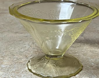 May include: A yellow glass footed bowl with a scalloped rim and a delicate floral pattern. The bowl is clear and has a vintage look.