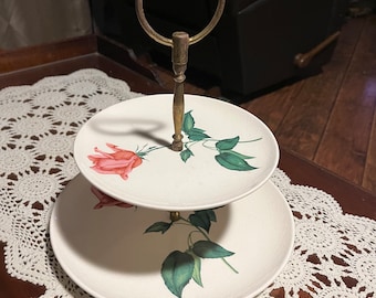 May include: Two-tiered white ceramic serving stand with a brass handle. The stand features a floral design with pink roses and green leaves.