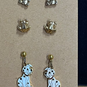 May include: A set of six gold-tone earrings featuring a pair of bear, frog, and Dalmatian dog designs. The Dalmatian dog earrings are dangle earrings with a gold-tone hook.