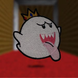 Könnte beinhalten: Gestickter Aufnäher mit einem Cartoon-Geist mit Krone. Der Geist ist weiß mit schwarzem Umriss, rosa Zunge und offenem Mund. Die Krone ist goldfarben mit roten und blauen Akzenten. Für Kleidung oder Accessoires.