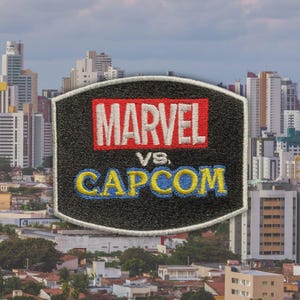 May include: A black patch with the words "MARVEL" in red and "CAPCOM" in blue and yellow, with "vs" in white between them. The patch is set against a cityscape background.