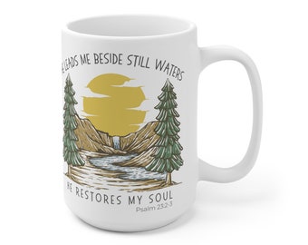 May include: White ceramic mug with a green and brown illustration of a mountain scene with a waterfall and a sun. The text reads "He leads me beside still waters He restores my soul Psalm 23:2-3."