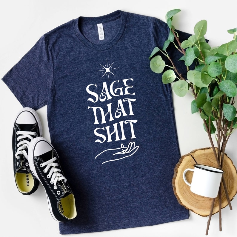 May include: A navy blue t-shirt with a white graphic that says "Sage That Shit" with a stylized hand holding a sprig of sage.