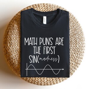May include: Black t-shirt with white text that reads "Math puns are the first sin(madness)" and a white sine wave graph.