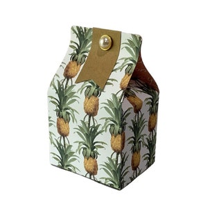 May include: A small white gift box with a brown paper tag and a pearl-like button. The box is decorated with a repeating pattern of pineapples and green leaves.