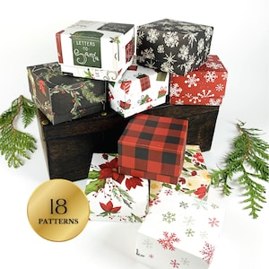 May include: A collection of small, square gift boxes with various holiday-themed patterns. Designs include snowflakes, plaid, poinsettias, and the text "Letters to Santa." The boxes are stacked on a dark wooden surface, with a gold emblem indicating 18 patterns.