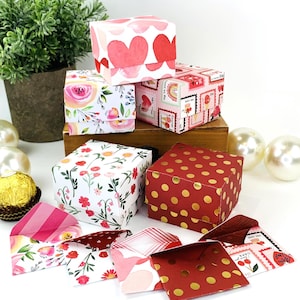 May include: Set of six small gift boxes with various Valentine's Day themed patterns. The boxes are made of cardboard and have a square shape. The patterns include hearts, flowers, and polka dots. The boxes are perfect for small gifts or favors.