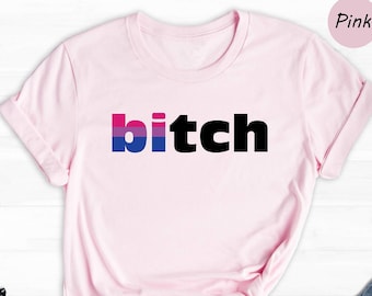 Puede incluir: Camiseta rosa con la palabra "bitch" en letras negras con un diseño de bandera bisexual.