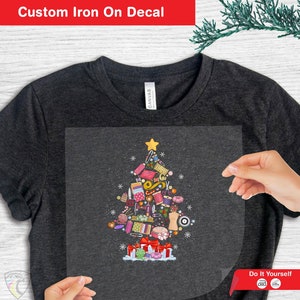 May include: Iron-on decal featuring a Christmas tree made of sewing supplies, including thread, scissors, buttons, and fabric. The decal is on a dark grey t-shirt. "Do It Yourself" is written at the bottom of the image.