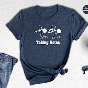 May include: A navy heather t-shirt with a white graphic of two stick figures holding musical notes. The text "Taking Notes" is printed below the graphic.