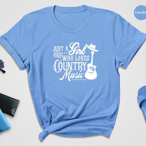 May include: Light blue t-shirt with a white graphic that says "Just a Girl... Who Loves Country Music" with a guitar and a cowboy hat.