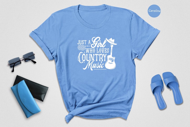 May include: Light blue t-shirt with a white graphic that says "Just a Girl... Who Loves Country Music" with a guitar and a cowboy hat.