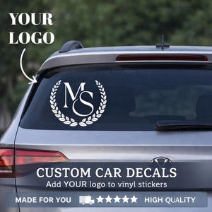 May include: White vinyl car decal featuring the letters "MS" within a laurel wreath design. The decal is displayed on a car's rear window. Text at the top says "YOUR LOGO" and at the bottom "CUSTOM CAR DECALS".