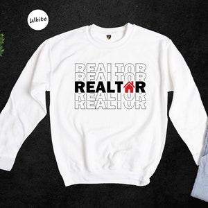 May include: White long-sleeved sweatshirt with the word "REALTOR" repeated four times in black text, with a red house icon in the middle "REALTOR".