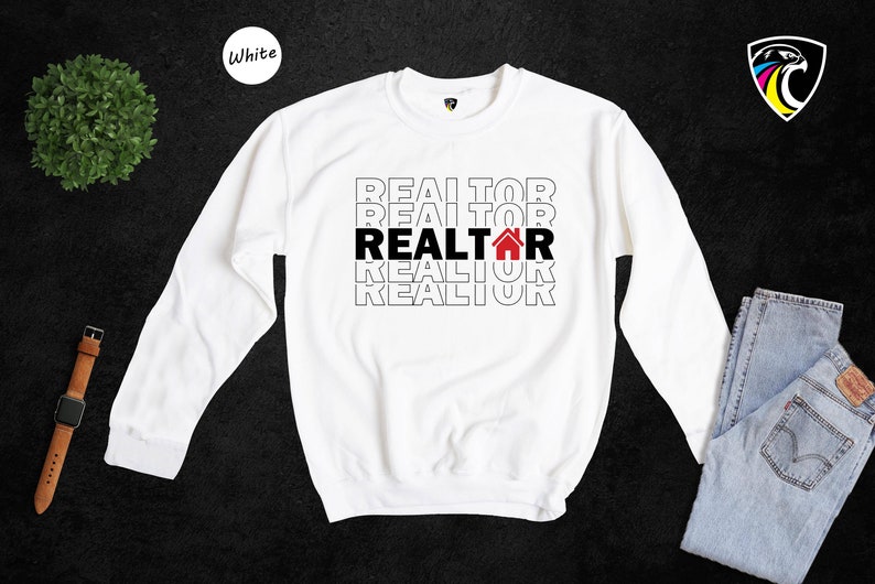 May include: White long-sleeved sweatshirt with the word "REALTOR" repeated four times in black text, with a red house icon in the middle "REALTOR".