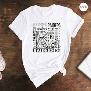 May include: White t-shirt with a black graphic design featuring the letter "R" surrounded by the word "Raiders" repeated multiple times.