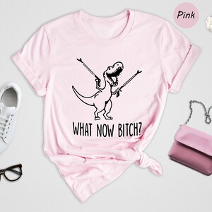 a pink t - shirt with a picture of a woman riding a dinosaur