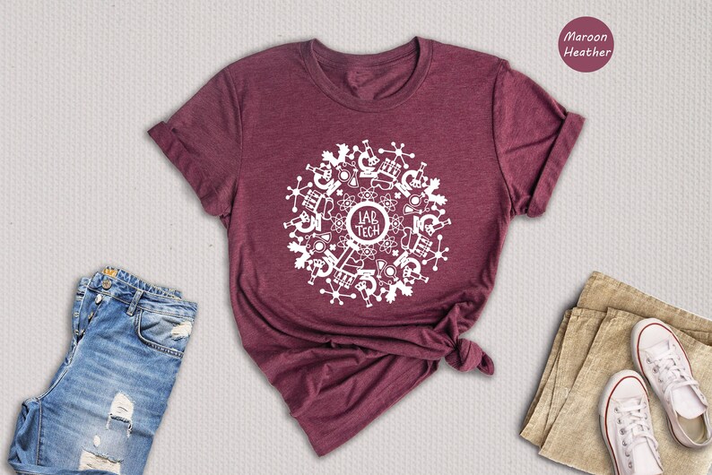 May include: A maroon heather t-shirt with a white design of a circle with science-related icons and the text "Lab Tech" in the center.