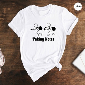 May include: White t-shirt with a graphic of stick figures holding musical notes and the text "Taking Notes".