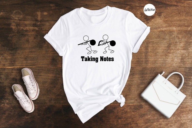May include: White t-shirt with a graphic of stick figures holding musical notes and the text "Taking Notes".