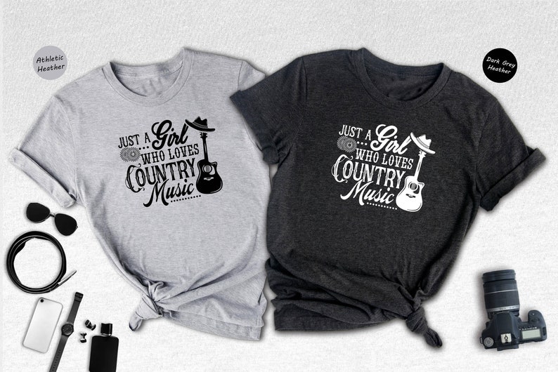 May include: Two t-shirts with a country music design. The gray t-shirt has black text and the dark gray t-shirt has white text. Both shirts feature a guitar and the text "Just a Girl Who Loves Country Music".