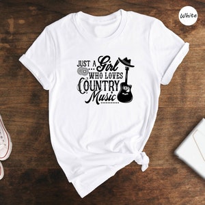 May include: White t-shirt with a black graphic that says "Just a Girl Who Loves Country Music" with a guitar and a cowboy hat.