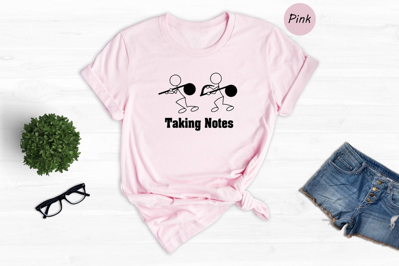 May include: Pink t-shirt with a graphic of two stick figures holding musical notes and the text "Taking Notes".