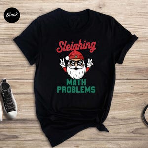 May include: Black t-shirt with a graphic of Santa Claus wearing sunglasses and saying "Sleighing Math Problems".