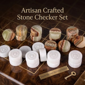 May include: Artisan Crafted Stone Checker Set. The image shows a checker set with stone checkers in shades of white, brown, and green. The checkers are arranged on a wooden surface. The text "Artisan Crafted Stone Checker Set" is at the top.