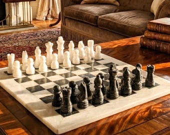 Può includere: Un set di scacchi in marmo con una scacchiera quadrata a riquadri alternati bianchi e neri. Il set include un set completo di pezzi degli scacchi intagliati in pietra bianca e nera, tra cui re, regine, alfieri, cavalli, torri e pedoni.