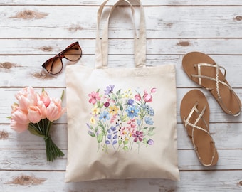 Könnte beinhalten: Eine weiße Canvas-Tragetasche mit einem Blumendesign mit rosa, blauen und gelben Blumen. Die Tasche hat lange Henkel und ist aus Naturstoff.