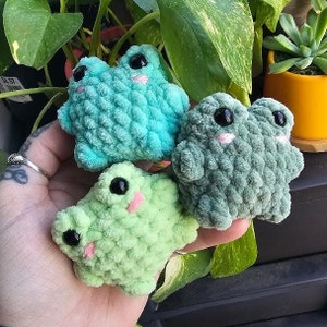 Puede incluir: Tres peluches de rana de crochet en diferentes tonos de verde. Las ranas tienen ojos grandes y est&aacute;n hechas con un hilo texturizado.