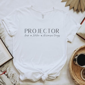May include: White t-shirt with black text that reads "PROJECTOR Guide + Intuitive + Alchemical Energy".