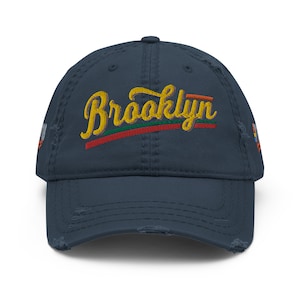 May include: A navy blue distressed baseball cap with a yellow embroidered word "Brooklyn" in a retro font with red and green accents.
