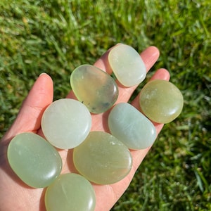 May include: A collection of eight smooth, polished green jade stones. The stones are various shades of green and have a natural, organic shape.