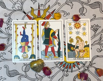 May include: Three tarot cards with colorful illustrations. The first card is titled "Le Pendu" and depicts a person hanging upside down. The second card is titled "Valet de Baton" and shows a person holding a staff. The third card is titled "Le Toille" and shows a person standing in a field with a star above them.