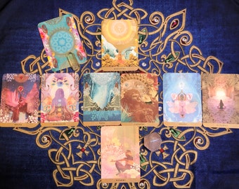May include: A spread of ten tarot cards on a blue background with a gold Celtic knot design. The cards feature colorful illustrations and text, including "MANIPURA", "KRIYA", "MULAADHARA", "VATA", "LAHSHMI", "CHAKRA", "VISHUDDHA", "SWADHISTHANA", "AJNA", and "Svadhisthana".