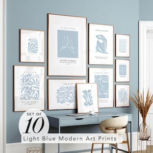 May include: A set of ten light blue modern art prints in various sizes, framed in gold. The prints feature botanical and abstract designs, including text that reads "Musée D'Orsay" and "William Morris". The prints are displayed on a light blue wall.
