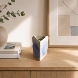 May include: A triangular ceramic vase with a smooth off-white finish featuring soft, blended gradients of blue and purple on its sides. The vase has a hollow centre and a distinct three-sided geometric shape, standing upright on a flat surface.