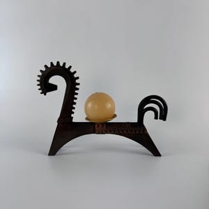 Puede incluir: Un portavelas en forma de caballo, de color marrón oscuro, con un diseño decorativo. El portavelas tiene una base circular y sostiene una vela redonda de color claro. El diseño recuerda al arte popular.