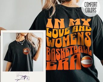 May include: Black t-shirt with the text "In My Love and Womens Basketball Era" in orange and yellow lettering with a basketball graphic. The text is in a retro font style.