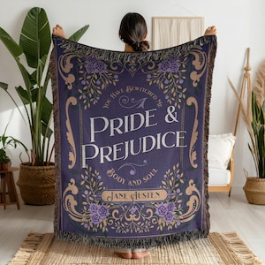 May include: A woven throw blanket in deep purple featuring the text Pride & Prejudice, You Have Bewitched Me, Body and Soul, and Jane Austen. The design includes ornate gold scrollwork and purple floral accents with a fringed edge on all sides.