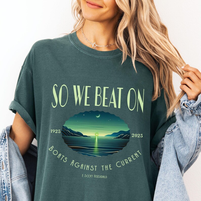 Comfort Colors 1717 classic tee in Blue Spruce — So We Beat On Fitzgerald quote tee with glowing green light bay scene and 1925–2025 centennial detail. Lifestyle shot, model wearing denim jacket. Ideal for readers, English majors, and classic literature lovers searching for bookish aesthetic apparel and Great Gatsby gifts.