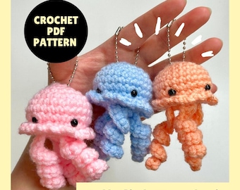 May include: Three crocheted jellyfish keychains in pink, blue, and peach. Each jellyfish has black eyes and dangling tentacles. The image includes the text "CROCHET PDF PATTERN" and "Jellyfish Keychain".