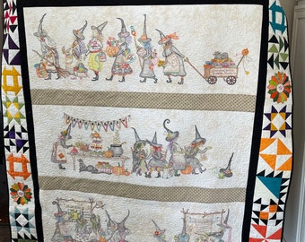 Könnte beinhalten: Eine große, handgefertigte Steppdecke mit Halloween-Motiv. Die Steppdecke zeigt Hexen, einen festlichen Tisch und eine Marktszene. Der Rand umfasst farbenfrohe geometrische Muster und florale Akzente, mit einem schwarzen Rand.